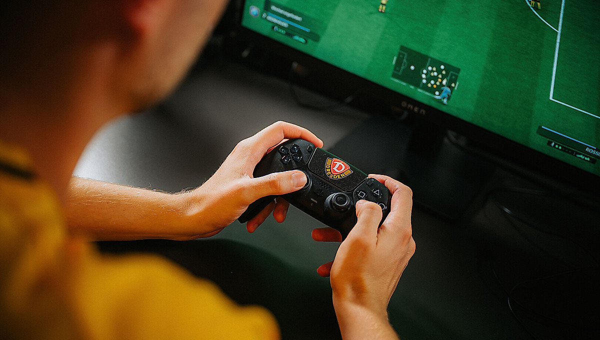 Ein eFußball hält den Controller der Playstation in der Hand.