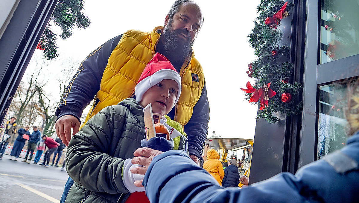 Ein Kind erhält einen vom Dynamo-Nikolaus befüllten Stiefel, dahinter steht sein Vater.
