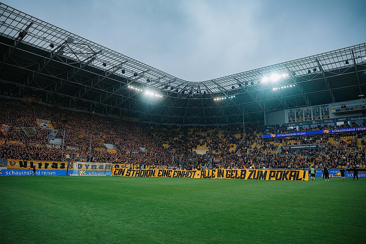 Die Spieler von Dynamo Dresden halten das Plakat hoch mit der Aufschrift: „Ein Stadion, eine Einheit - Alle in Gelb zum Pokalspiel“