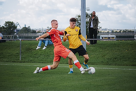 Ein Dynamo-Spieler dribbelt mit dem Ball an einem grätschenden Gegenspieler vorbei.