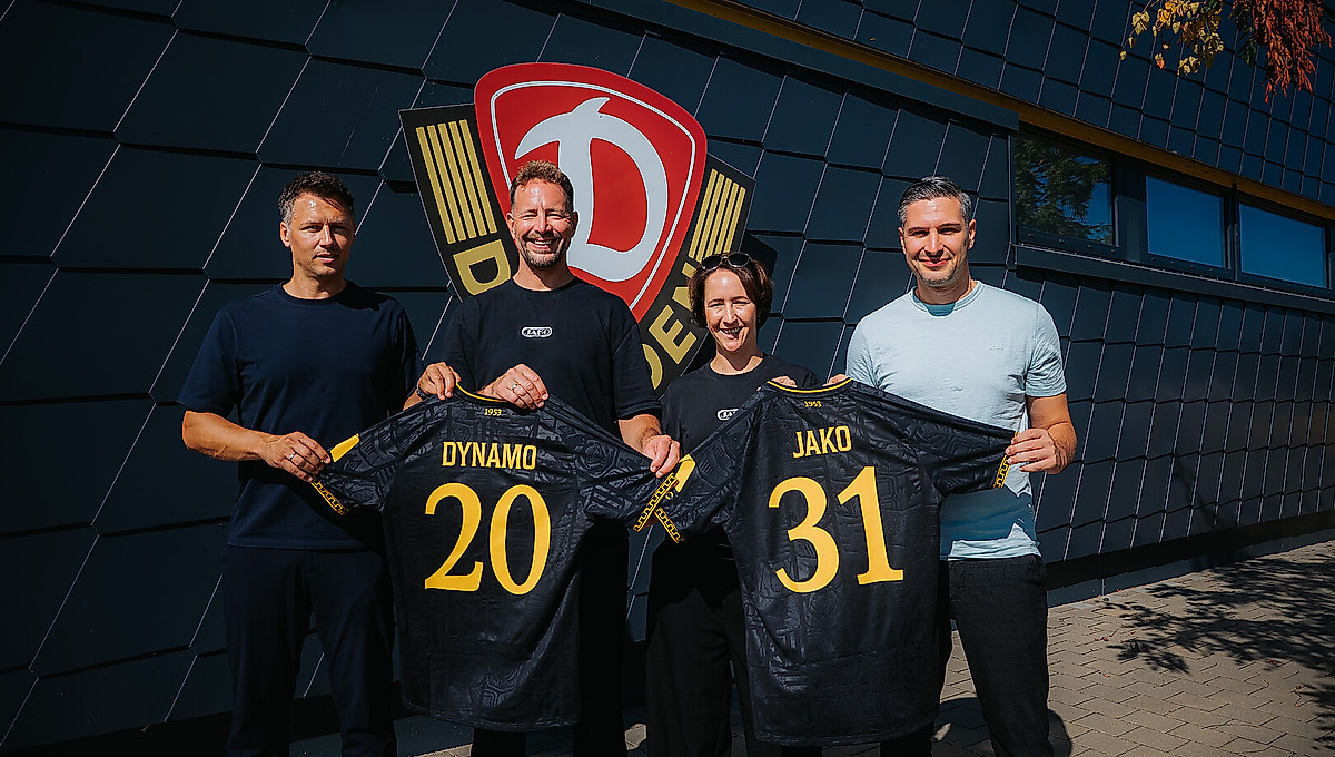 Sören Gonther (Sportgeschäftsführer SGD), Tobias Röschl (Vorstand Marketing & Vertrieb JAKO), Nadine Sprügel (Vorstandsvorsitzende JAKO) und Stephan Zimmermann (Geschäftsführer SGD) halten gemeinsam zwei aktuelle Auswärtstrikots der Sportgemeinschaft hoch. Auf den Trikots ist anhand der Rückennummern die Zahl 2031 zu lesen.