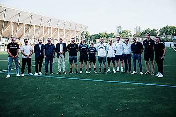 Die Geschäftsführung der SGD steht zusammen mit Vertretern aller beteiligter Vereine und dem geladenen Sächsischen Innenminister Armin Schuster und Sportbürgermeister Jan Donhauser auf dem neuen Kunstrasenplatz am Rudolf-Harbig-Stadion.