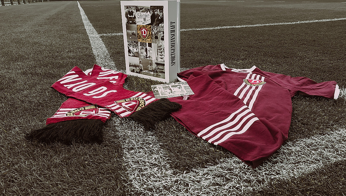 Der Schal, die Postkarte und das Trikot der weißen Retro-Box auf dem Rasen an der Markierung der Eckfahne.