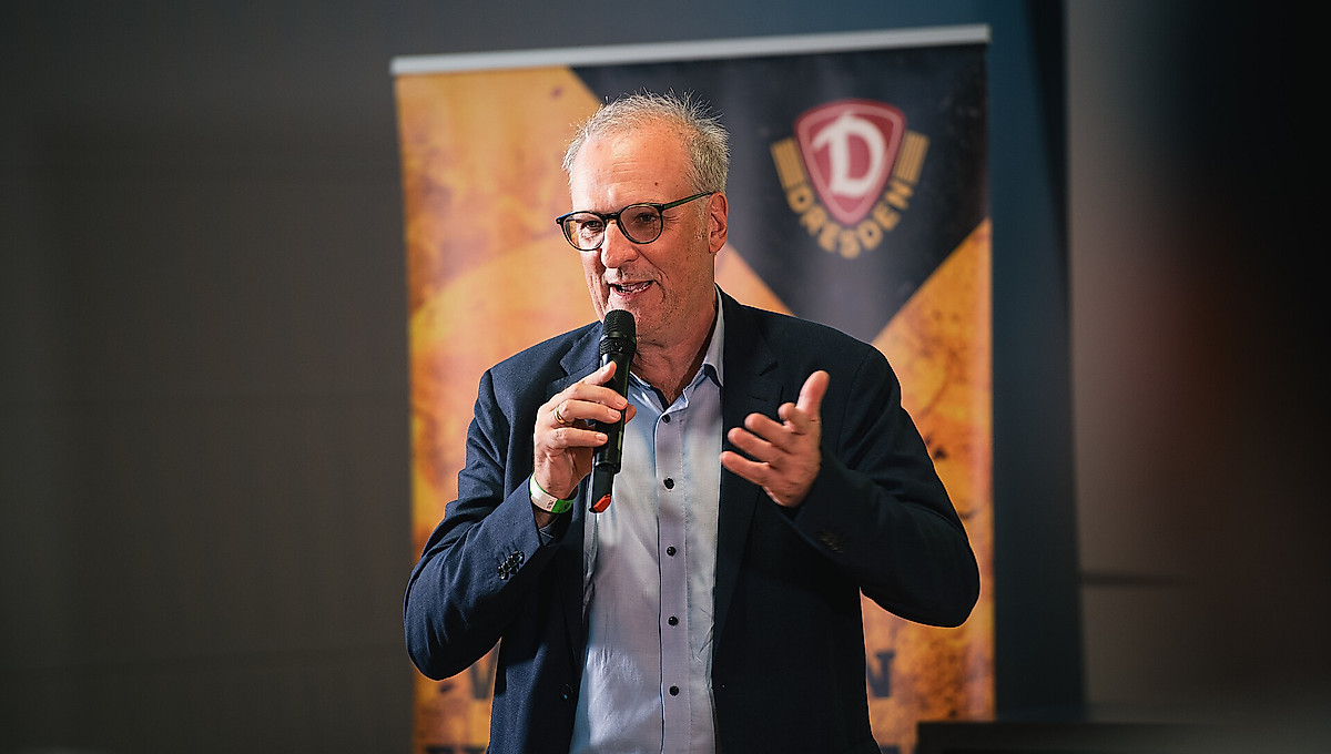 Dr. Jürg Kasper mit einem Mikrofon in der Hand bei einer Mitgliederveranstaltung.