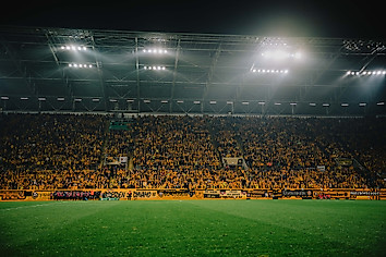 Rasen und besetzte Westtribüne unter Flutlicht im Rudolf-Harbig-Stadion.