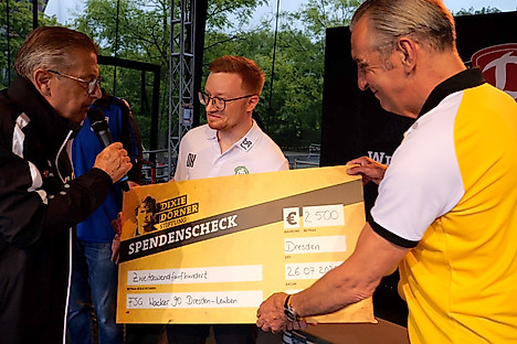 Ralf Minge überreicht auf der Bühne einen Spendenscheck an den FSV Wacker Leuben. Das war bei der Saisoneröffnung von Dynamo Dresden.