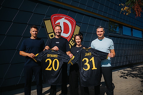 Sören Gonther (Sportgeschäftsführer SGD), Tobias Röschl (Vorstand Marketing & Vertreib JAKO), Nadine Sprügel (Vorstandsvorsitzende JAKO) und Stephan Zimmermann (Geschäftsführer SGD) halten gemeinsam zwei aktuelle Auswärtstrikots der Sportgemeinschaft hoch. Auf den Trikots ist anhand der Rückennummern die Zahl 2031 zu lesen.