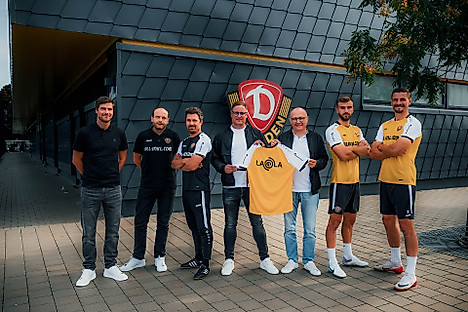 Dynamos Geschäftsführer David Fischer, Cheftrainer Thomas Stamm und die SGD-Spieler Lars Bünning und Stefan Kutschke posieren mit den neuen Teampartnern der Profis vor dem Dynamo-Wappen am Funktionsgebäude im Trainingszentrum der SGD.
