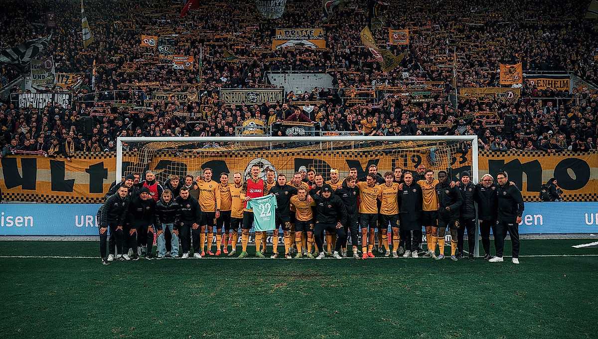 Mannschaft und Staff der SGD halten im Tor vor dem K-Block ein Trikot von Torhüter Lennart Grill hoch..