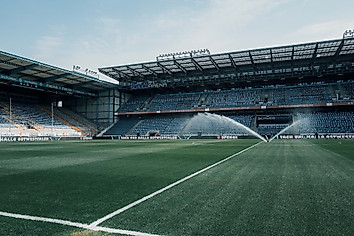 Das Stadion der Schüco-Arena mit leeren Rängen und einem laufenden Rasensprenger vor der Stadionöffnung.