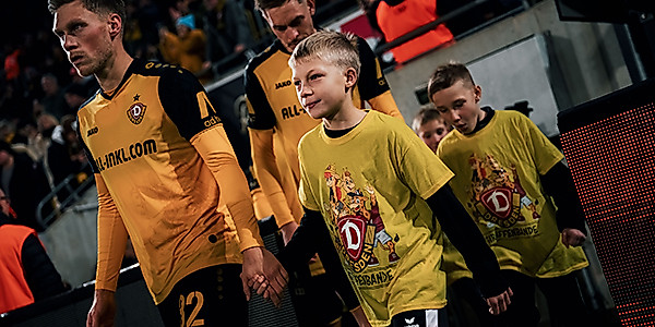 Giraffenbanden-Kind läuft an der Hand eines Dynamo-Spielers im Stadion ein