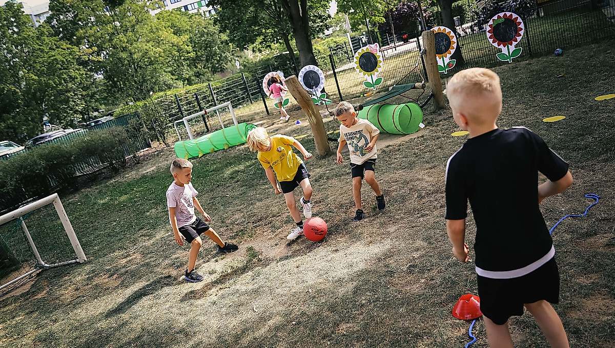 Kinder spielen auf einem Spielplatz mit einem Ball.