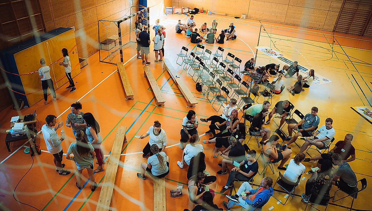 Eine Turnhalle in der sich viele Menschen versammelt haben