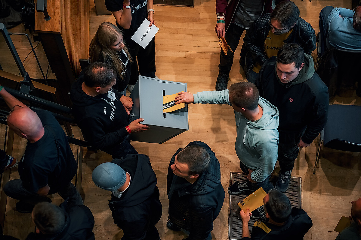 Menschen stecken Zettel in eine Wahlurne.