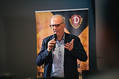 Dr. Jürg Kasper mit einem Mikrofon in der Hand bei einer Mitgliederveranstaltung.