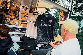 Ein Mann begutachtet die Dynamo-Auswärtstrikots der Saison 2025/26 vor einem Dynamo-Fanshop-Verkaufsstand.