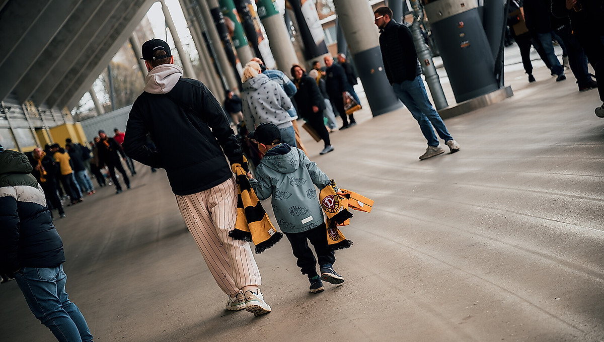 Ein Vater und ein Kind im Stadion, von hinten fotografiert.