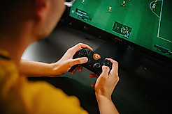 Ein eFußball hält den Controller der Playstation in der Hand.