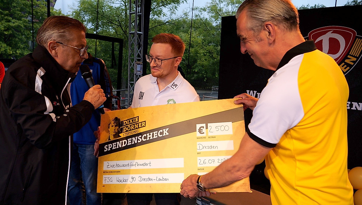Ralf Minge überreicht auf der Bühne einen Spendenscheck an den FSV Wacker Leuben. Das war bei der Saisoneröffnung von Dynamo Dresden.