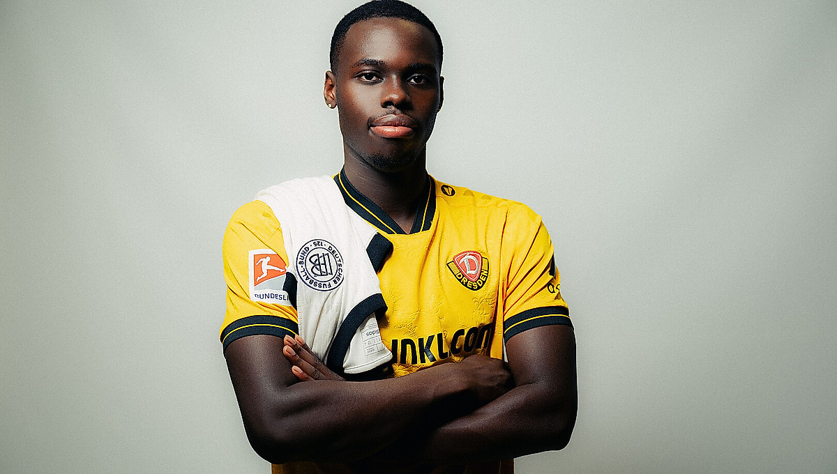 Kofi Amoako im Dynamo-Trikot mit einem Trikot der deutschen Nationalmannschaft über der Schulter.