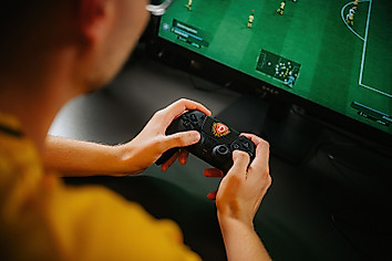 Ein eFußball hält den Controller der Playstation in der Hand.