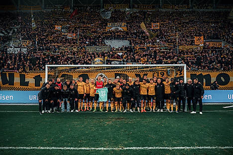 Mannschaft und Staff der SGD halten im Tor vor dem K-Block ein Trikot von Torhüter Lennart Grill hoch..